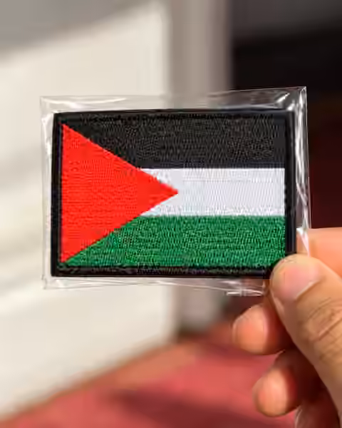 Neatly presented embroidered Palestinian flag patch in a transparent sleeve, held by hand